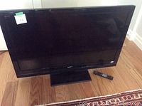 Front view of Sony Bravia 46-inch LED TV with remote placed next to the base stand on hardwood flooring, showing the display and physical condition.