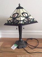 Photo of Tiffany style table lamp unlit, showing stained glass shade and metal base with pull chains visible.