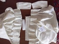 Two white IKEA Anita drape panels with sewn goblet pleats and fabric ties and iron-on hem pieces on a wooden surface.