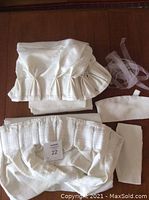 Two folded white fabric drape panels with sewn goblet pleats, tiebacks, and iron-on hem strip laid out on wooden surface