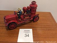 Front angled view of the red cast iron toy fire truck with seated firefighter figure, showing intricate details of the engine and fire equipment.