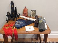 Collection of Asian craft items on a small table including plate holders, tassels, mask, fan, chopsticks, and boxed perfume bottle.