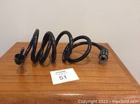 Coiled black combination cable lock with visible combination dial and cable ends on a wooden surface with a lot tag.