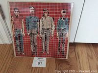 Front cover of Talking Heads 'More Songs About Music and Food' vinyl LP, showing the four band members in front of a red grid background on a square album cover.