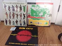 Lot of 3 vinyl LPs shown standing against a white door on hardwood floor. Visible albums: King Sunny Ade and his African Beats 'Synchro System', Hugh Masekela 'Techno-Bush', and Artists United Against Apartheid 'Sun City'.