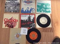 Top-down photo showing 8 vinyl 45 records with a variety of label colors and cover art on wooden floor.