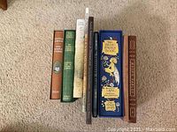 Photo shows an array of 8 books standing upright, includes titles by Agatha Christie, The Secret Garden, The Judge Fairy Book, and others, with varied bindings including folio editions and decorative covers.