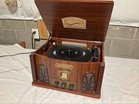 Front angled view of the Nostalgia record player and radio showing the open lid, turntable platter, tonearm, and wood grain wooden cabinet.