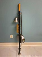 Full view of a one man band instrument showing the vertical black pole with attached bell, drum, and wooden handle.