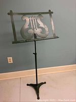 Full view of the green painted iron music stand showing the lyre design on the music holder and tripod base.