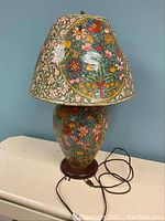 Front view of the floral motif lamp with matching shade showing colorful rawhide-like material and plugged electrical cord.