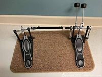 Top down view of Ludwig double kick pedal on brown carpet, showing footboards with white stripes and Ludwig logo.