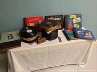 Wide view of vintage 78 RPM records stacked on a table alongside colorful album jackets and cases displaying names like Charlie Christian and Les Brown.