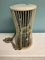 Full drum angled view showing black body, natural drumhead, white rope tuning and attached fabric strap.