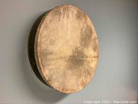 Side view of frame drum showing natural drumhead with signs of use, mounted on a wall.