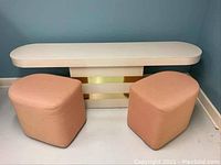 Front view of white coffee table vanity and two peach upholstered stools against a blue wall.