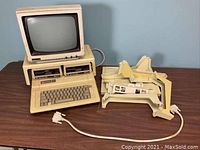 Apple IIe main unit with keyboard, two floppy drives mounted on top, CRT monitor on left and pile of plastic risers on right