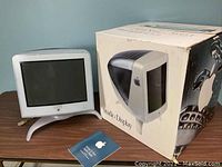 Apple 17-inch Studio Display CRT monitor displayed alongside original box and setup manual on wooden table.