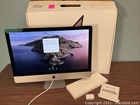 Front view of powered-on iMac with keyboard and trackpad boxes and adapter displayed