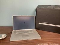 Photo of the open Apple PowerBook G4 laptop on a table next to its original box