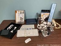 Wide shot of assorted Mac accessories and miscellaneous household electronics arranged on a table including keyboards, charging cables, cordless phones, and a monitor stand.