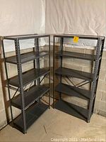 Two black metal shelving units standing on the floor side by side in a basement corner, showing front and side views.