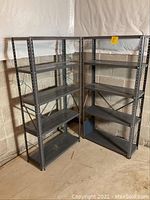 Two full metal shelving units side by side against basement wall.