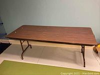 Full view of fold-down event table showing rectangular wood grain laminate top and brown metal legs