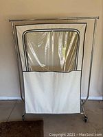 Front view of rolling metal clothes rack with beige fabric clothes bag having a large clear plastic window on the front.