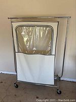 Front view of rolling metal clothes rack with white protective bag featuring a clear plastic window.
