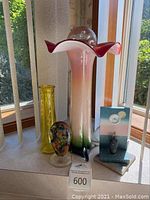 Overview photo showing all four glass art pieces on window ledge: tall flared vase, yellow vase, colorful paperweight, decorative clock with glass art stand