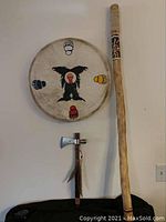 Group shot of drum front mounted on wall with tomahawk and walking stick standing below