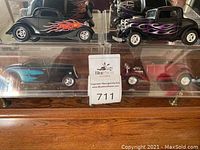 Front and top views showing the black coupe with red and orange flames and the black coupe with purple flames, along with other cars on acrylic display riser.