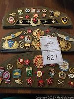 Three olive drab side caps laid flat showing various enamel pins and metal badges