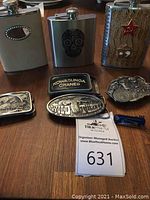 Group view of three flasks, four belt buckles and tie tac on wooden surface