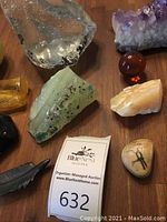 Overview of multiple stones, including polished ambers, greenish stone with dark marks, and rough amber-yellow chunks.