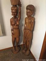 Both wooden tribal carvings displayed side by side in corner