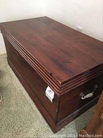Photo showing closed wooden hope chest with decorative trim and metal handle on side
