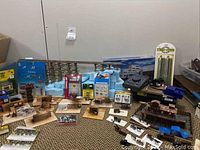 Wide view of the entire lot showing a collection of miniature wooden fences, a boxed electronic control unit, multiple packs of miniature animals and figures, and train track and bridge components.