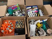 Four cardboard boxes filled with various art supplies, including bottles, brushes, and holders.