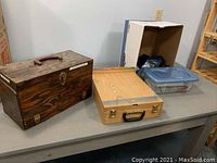 Three carrying cases on table: wooden pyrography case, light woodgrain case, plastic tub