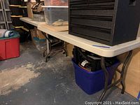 View of plastic topped folding table with metal legs and storage items under it.