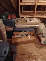 Three plastic tubs and one cardboard box containing assorted Christmas decorations and lighting, stored in an attic space