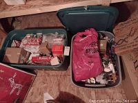 Overview of two green plastic bins filled with Christmas decorations including boxes, a pink bag, and assorted items