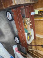 Red wooden wagon viewed diagonally showing contents inside including horseshoes and paddles.