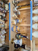 Overview of a wooden table with porcelain teacups, saucers, pitchers, and other assorted porcelain items arranged neatly, showing the blue and gold decorative style.