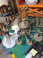 Overhead view of chandelier on green tarp with attached tag, showing eight arms and black sleeves