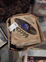 Photo of a box containing multiple vintage 78 RPM Decca records in original paper sleeves.