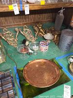 Photo shows two mantle clocks, three cherub styled wall sconces in brass or gold-color, two small glass candle holders, a small decorative tin container, and a Czech seltzer bottle with textured metal top.