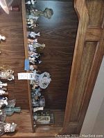 Multiple ceramic animal figurines including cats, bears, rabbits, and chickens displayed on a wooden shelf along with a white ceramic knick knack shelf.